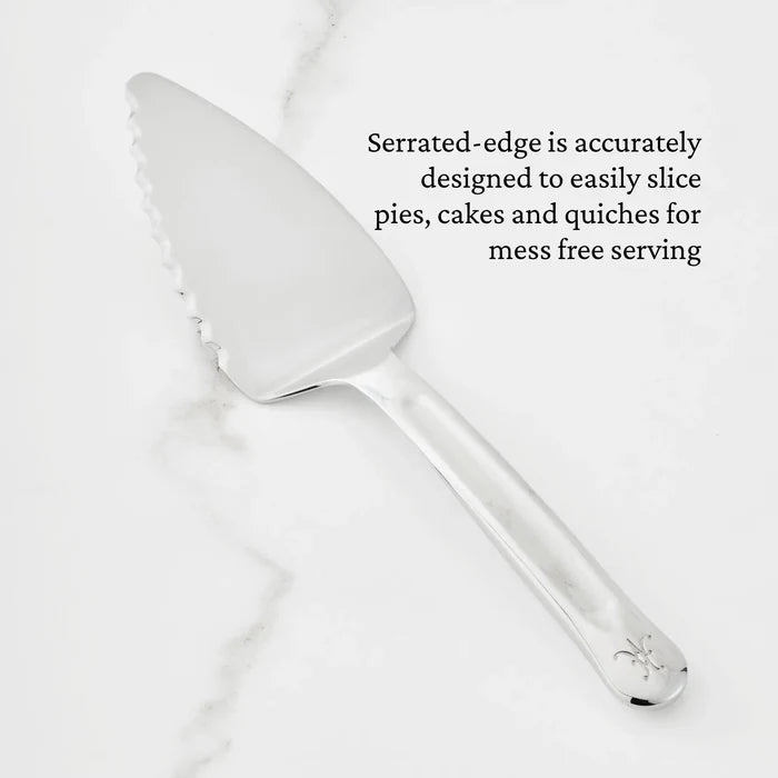 A Hestan Provisions® 10.5-inch Stainless Steel Pie & Cake Server with a serrated edge is displayed on a white marble surface. Text reads: The precisely crafted serrated edge easily slices pies, cakes, and quiches for mess-free serving—a perfect addition to your Provisions Serving Tools collection.