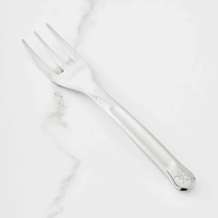 A 10.5-inch Stainless Steel Serving Fork from Hestan Provisions® rests on a white marble surface. Featuring three wide tines and a handle with a small engraved design near the end, this serving fork is an essential addition to any chef’s toolkit.