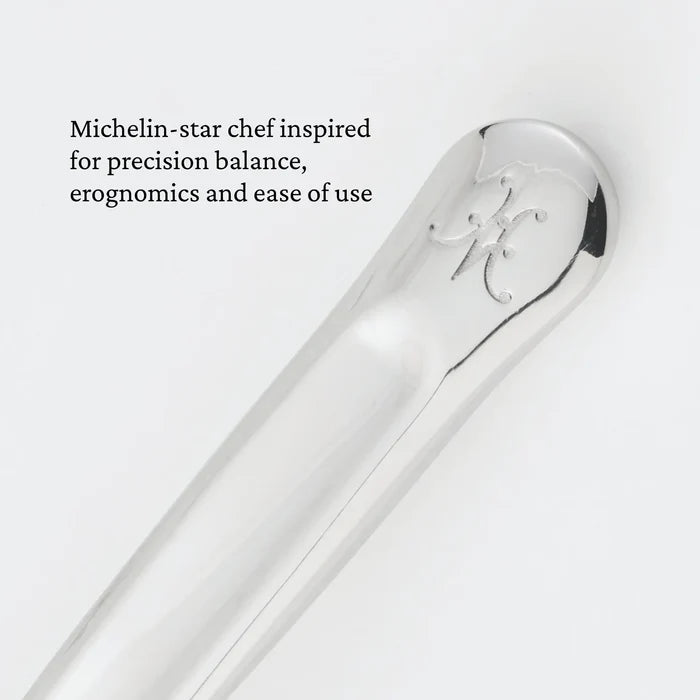 Close-up of a polished metal utensil handle engraved with an ornate letter. Text beside it reads: Michelin-star chef inspired for precision balance, ergonomics, and ease of use—experience the difference with the Hestan Provisions® 10.5-inch Stainless Steel Solid Serving Spoon, expertly crafted as an essential chef’s tool for every kitchen.