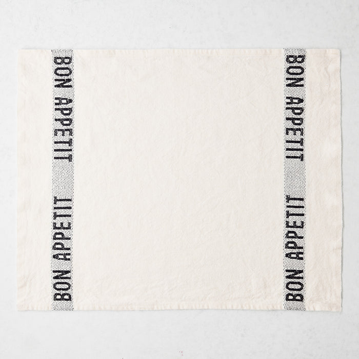 White linen napkin with "BON APPETIT" in black lettering on two vertical stripes.