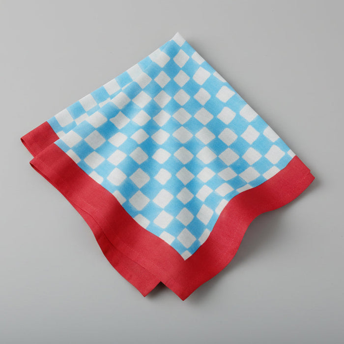 Blue check cotton voile napkin with a red border, 20" square.