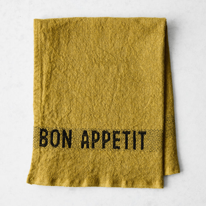 Goldenrod linen napkin with "BON APPETIT" in black lettering, folded on a white surface.