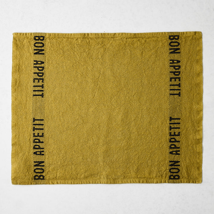 Goldenrod linen napkin with "BON APPETIT" in black text on two vertical sides.