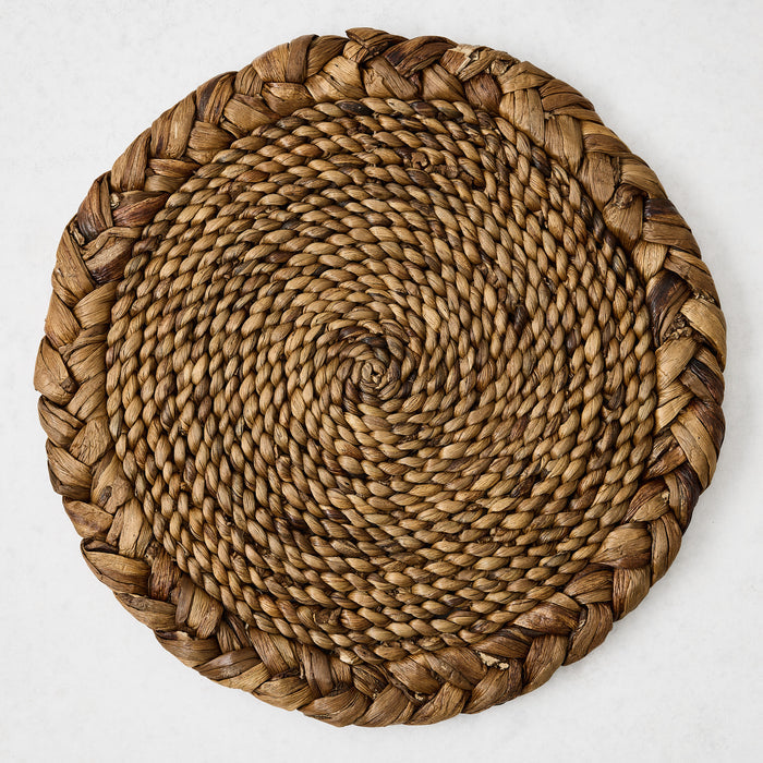 16-inch round braided water hyacinth placemat in honey-brown with a textured spiral center and thick woven border.