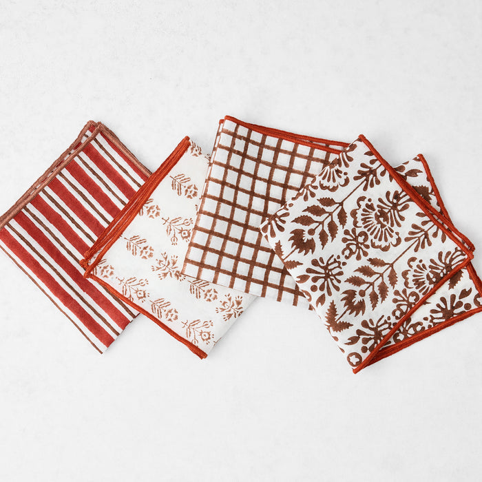 Set of four 10-inch cotton appetizer napkins with brick red and camel brown block print patterns and embroidered edges.