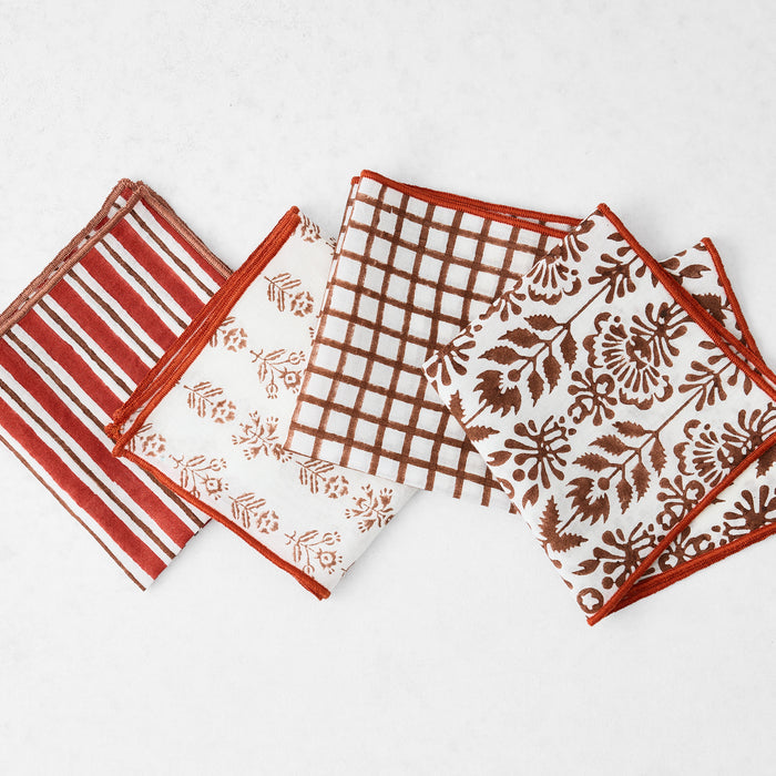 Set of four 10-inch cotton appetizer napkins in brick red and camel brown block prints with embroidered edges.