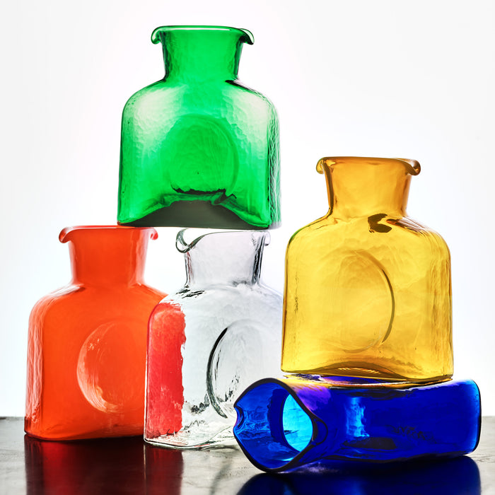 Stack of five textured square glass pitchers in green, yellow, orange, clear, and blue.
