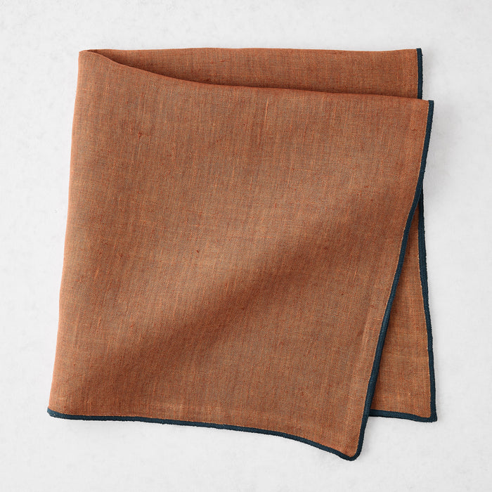 22-inch square camel brown linen napkin with a contrasting navy blue embroidered tipped stitch edge.