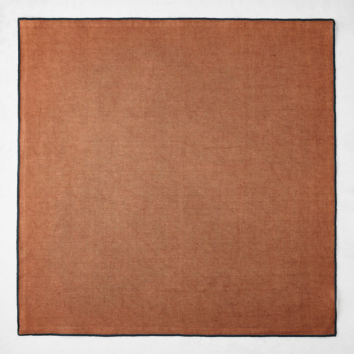 22-inch square camel brown linen napkin with a contrasting navy blue embroidered tipped edge.