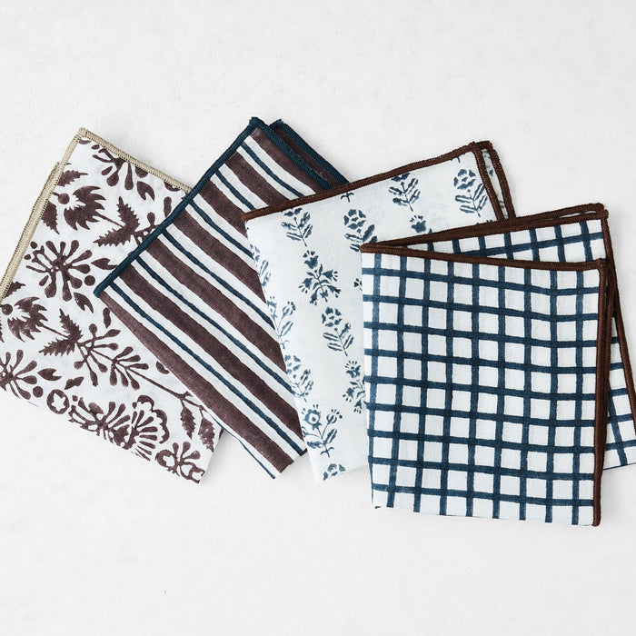 Set of four 10-inch cotton appetizer napkins with assorted chocolate and navy block print patterns and embroidered edges.