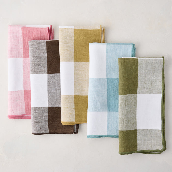 Five folded 20" x 20" linen napkins in buffalo check: pink, chocolate brown, mustard, light blue, and olive green.