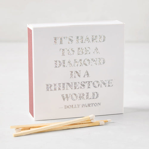 Square white matchbox with holographic text reading It's Hard to be a Diamond in a Rhinestone World by Dolly Parton.