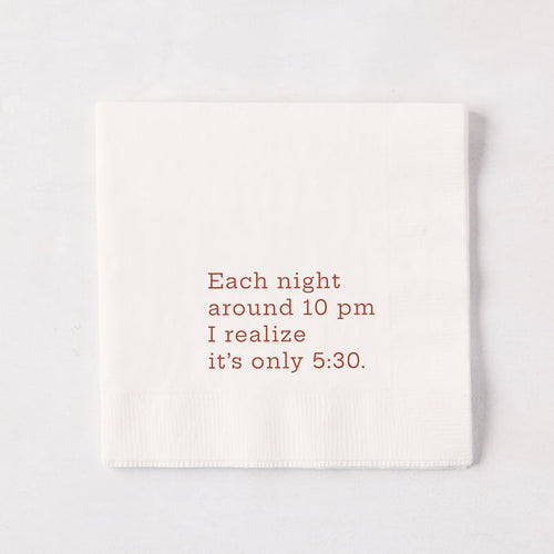 White 5.5-inch square 3-ply paper cocktail napkin with brown text reading Each night around 10 pm I realize it’s only 5:30.