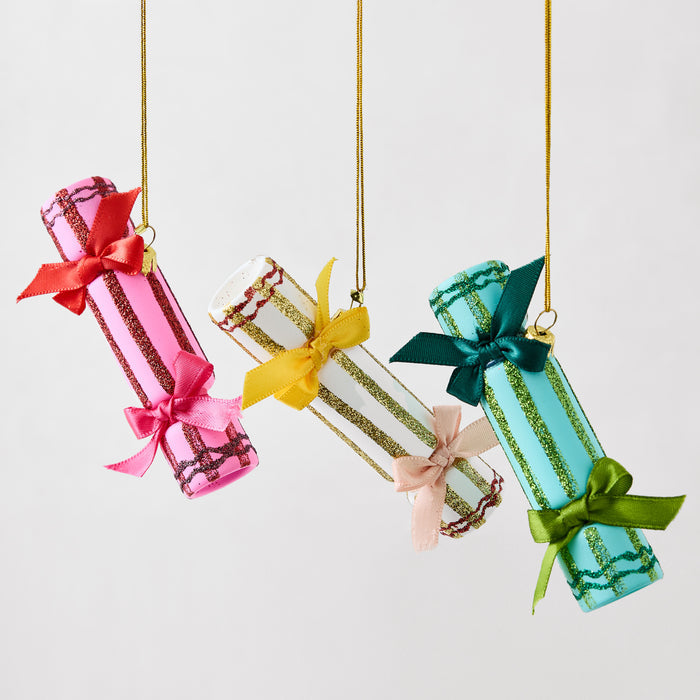 Three hanging Christmas cracker ornaments in pink, white, and green with glittered stripes and silk ribbon bows.