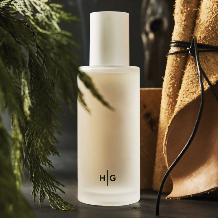 Hudson Grace Bleecker Room Spray in a minimalist frosted glass bottle with HG logo, surrounded by greenery and leather.