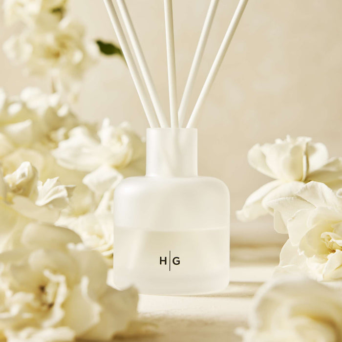 Hudson Grace Greenwich Scented Room Spray in a frosted glass bottle with white reeds, surrounded by gardenias.