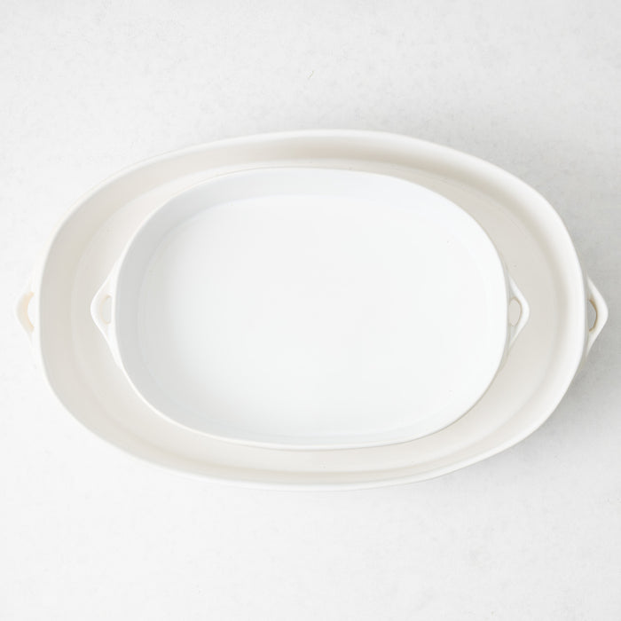 Large white oval stoneware baker with small side handles, viewed from above on a light background.