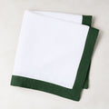 Folded white linen napkin with a fir green border.