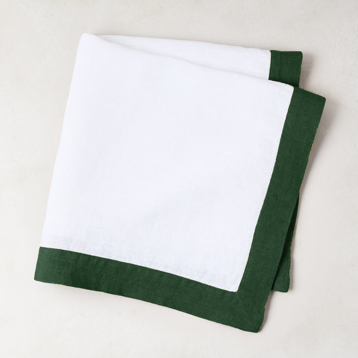 Folded white linen napkin with a fir green border.