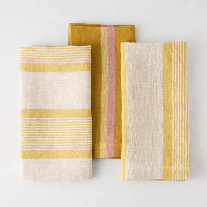 Three folded Madras cotton napkins with marigold, pink, and natural stripes.