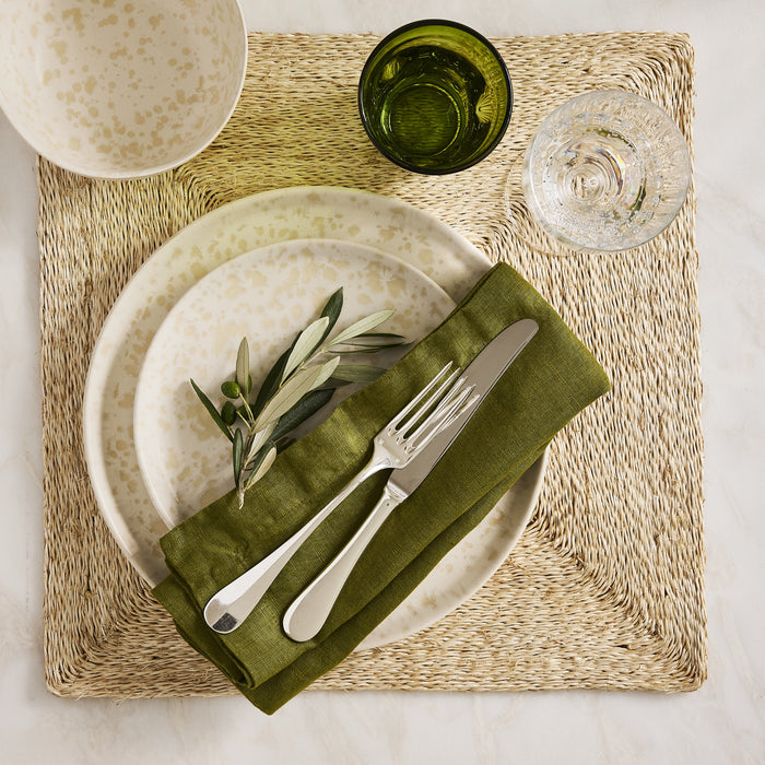 11-inch cream stoneware dinner plate with beige splatter pattern, styled with a green linen napkin and olive branch.