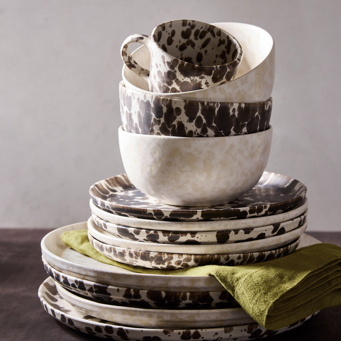 Stack of cream stoneware salad plates and bowls with a brown splatter pattern, accented by a green linen napkin.
