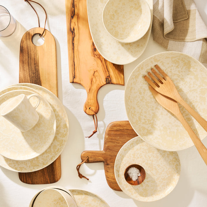 Natural Nuno Splatter Stoneware Mug with beige spots on cream, part of a full dinnerware set and wood boards.