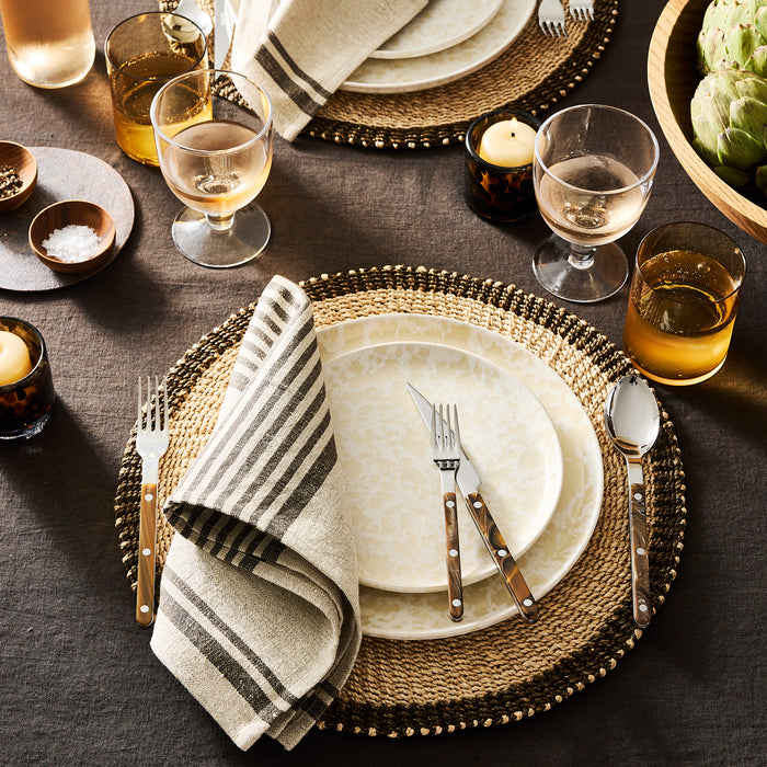 Natural Nuno Splatter stoneware salad plate with unique beige spots on a pale cream base, set on a woven placemat.