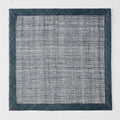 Navy blue square placemat made of woven abaca fibers with a semi-transparent center and solid border.