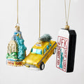 Hand-painted glass NYC Christmas ornaments featuring a skyline, yellow taxi, and JFK luggage tag with glitter accents.