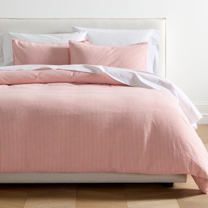 Orange seersucker stripe cotton Euro shams and duvet cover on a bed with white sheets.