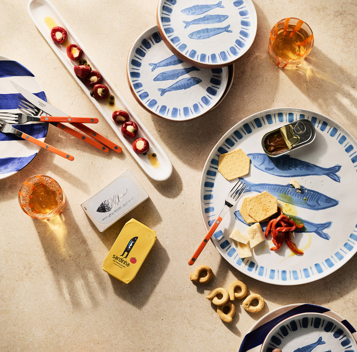 Blue Sardine terracotta serving platter with fish design, small plates, and appetizers on a beige surface.