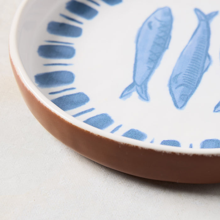 Round terracotta serving platter with white glaze and blue painted sardine design.