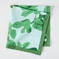 Pale blue cotton slub napkin with bold green fig leaf print and a solid green border.