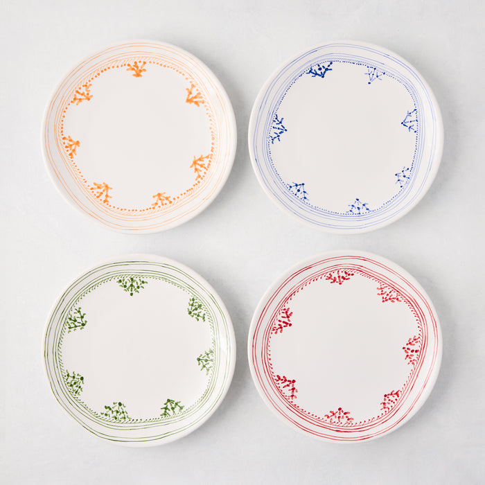 Four white appetizer plates with hand-painted borders: orange, blue, green, and red patterns.