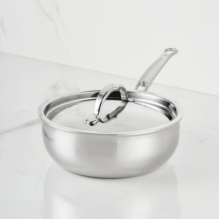 A ProBond Luxe® Polished Clad Stainless Steel Saucier Pan, 2-Quart, with a matching lid sits on a white marble countertop. This professional cookware features a long, ergonomic handle and a shiny, reflective finish.