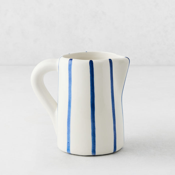 Small Portofino ceramic pitcher with white glaze, hand-painted blue vertical stripes, curved handle, and spout.