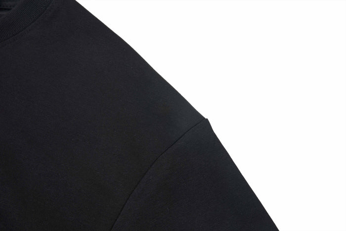 Close-up of a black streetwear T-shirt sleeve and shoulder seam on a white background