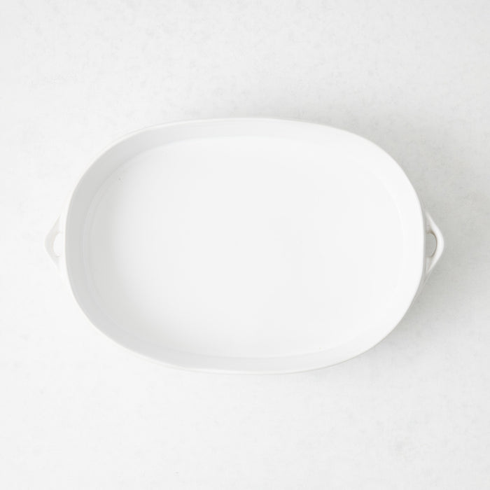 Small white oval stoneware baker with side handles, viewed from above on a light background.