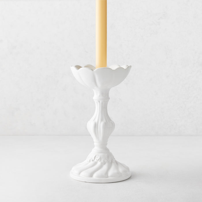 Small Tosca white ceramic candlestick with a scalloped top and elegant pedestal base holding a taper candle.