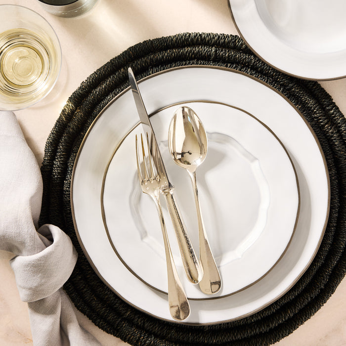 Smoke Grey Stoneware Petal Salad Plate with silver rim, fork, knife, and spoon on a dark woven placemat.