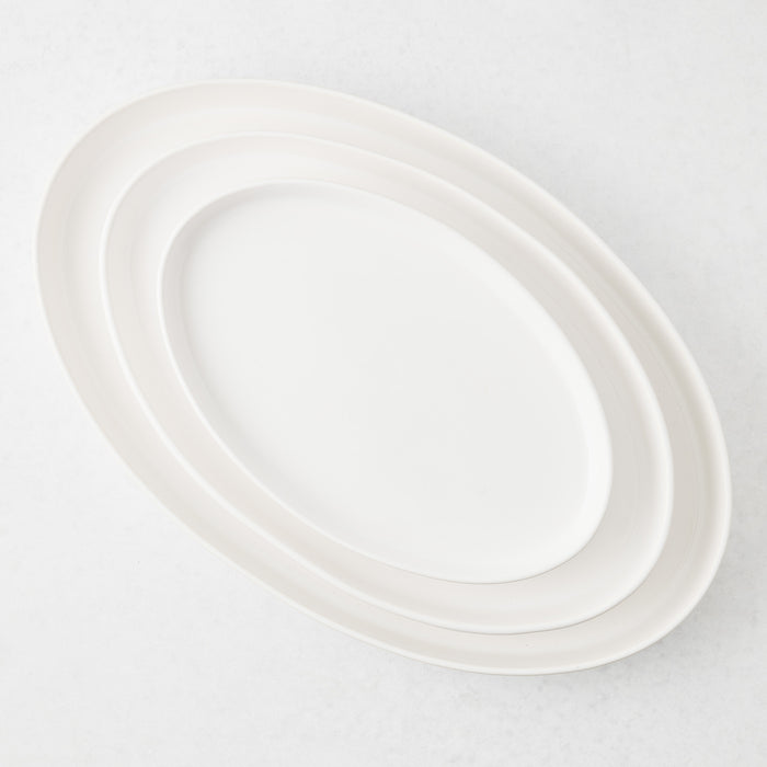 Three nested, oval-shaped white stoneware platters with a smooth, minimalist design on a light background.