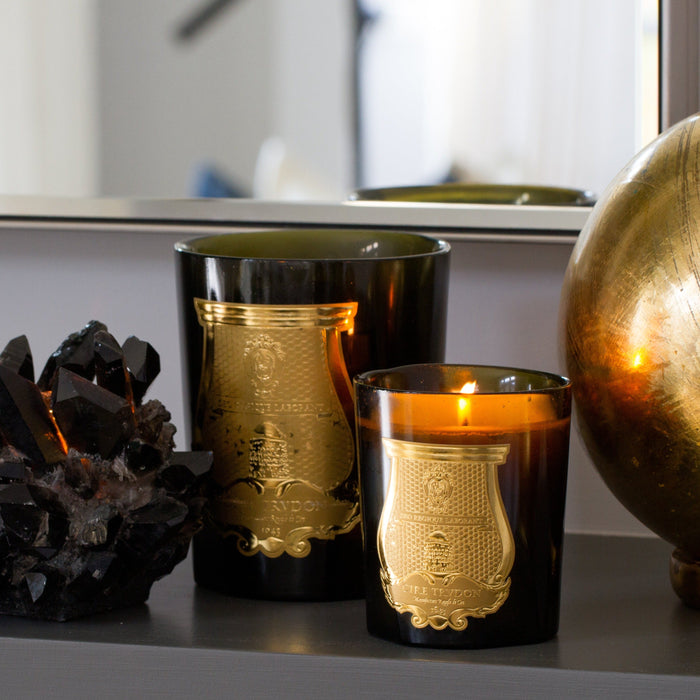 Two Trudon Tuileries scented candles in dark glass vessels with gold labels, one lit.