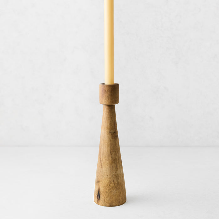 Hand-carved walnut wood candlestick with a geometric tapered base and a cream taper candle on a white background.